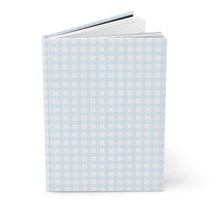 May include: A light blue book with a white gingham pattern on the cover. The book is closed and the pages are slightly fanned out.