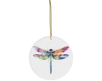 May include: A round white ornament featuring a watercolor dragonfly design. The dragonfly has colorful wings in shades of pink, blue, green, and yellow. A gold string is attached for hanging.