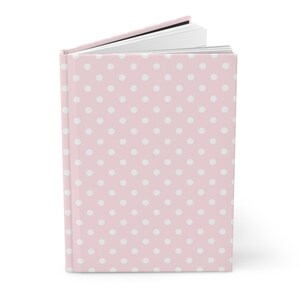 Könnte beinhalten: Ein rosa Hardcover-Journal mit einem weißen Polka-Dot-Muster.
