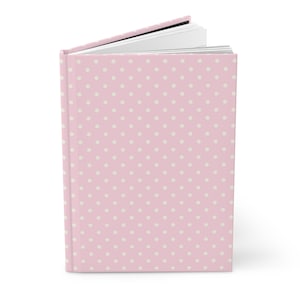 Könnte beinhalten: Ein rosa Notizbuch mit weißem Punkte-Muster. Das Notizbuch ist geschlossen und die Seiten sind leicht geöffnet.