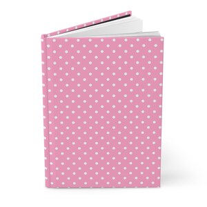 Könnte beinhalten: Ein rosa Notizbuch mit weißen Punkten. Das Notizbuch ist geschlossen und der Einband ist sichtbar.