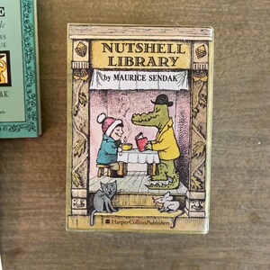 May include: A rectangular book titled Nutshell Library by Maurice Sendak, published by HarperCollinsPublishers. The cover features a color illustration of a child and a crocodile at a table, with a cat and a mouse below, framed by decorative borders.