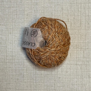 May include: A ball of Classic Cotton Jeans yarn in shades of brown and tan. The yarn has a textured appearance and a label that reads "Cotton Jeans" and "CLASSIC". Ideal for knitting and crochet projects.