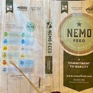 May include: A white bag of NEMO FEED animal nutrition with a brown and green logo. The bag is labelled with the text "Commitment to Quality" and "www.nemofeed.com". The bag is 50 pounds (22.7 kg).