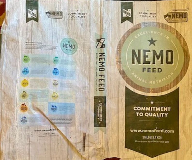 May include: A white bag of NEMO FEED animal nutrition with a brown and green logo. The bag is labelled with the text "Commitment to Quality" and "www.nemofeed.com". The bag is 50 pounds (22.7 kg).
