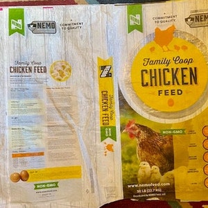 May include: A white bag of chicken feed with a yellow label. The label says "Family Coop Chicken Feed" and "Non-GMO". The bag is 50 lb (22.7 kg).