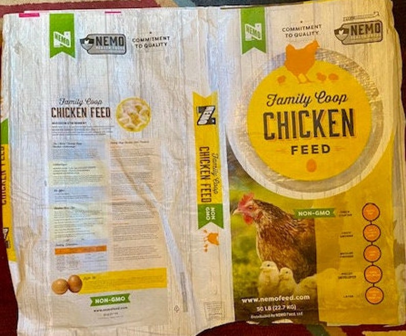 May include: A white bag of chicken feed with a yellow label. The label says "Family Coop Chicken Feed" and "Non-GMO". The bag is 50 lb (22.7 kg).