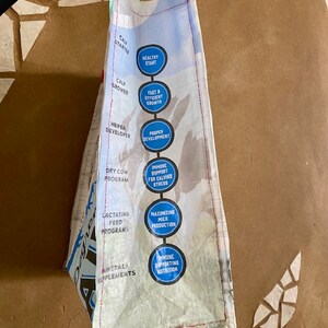 May include: A white bag with blue circles containing text about different stages of cow development. The text includes "Calf Starter", "Healthy Start", "Fast & Efficient Growth", "Proper Development", "Dry Cow Programme", "Immune Support for Calving Stress", "Lactating Feed Programmes", "Maximizing Milk Production", "Mineral Supplements", and "Immune Supporting Nutrition".