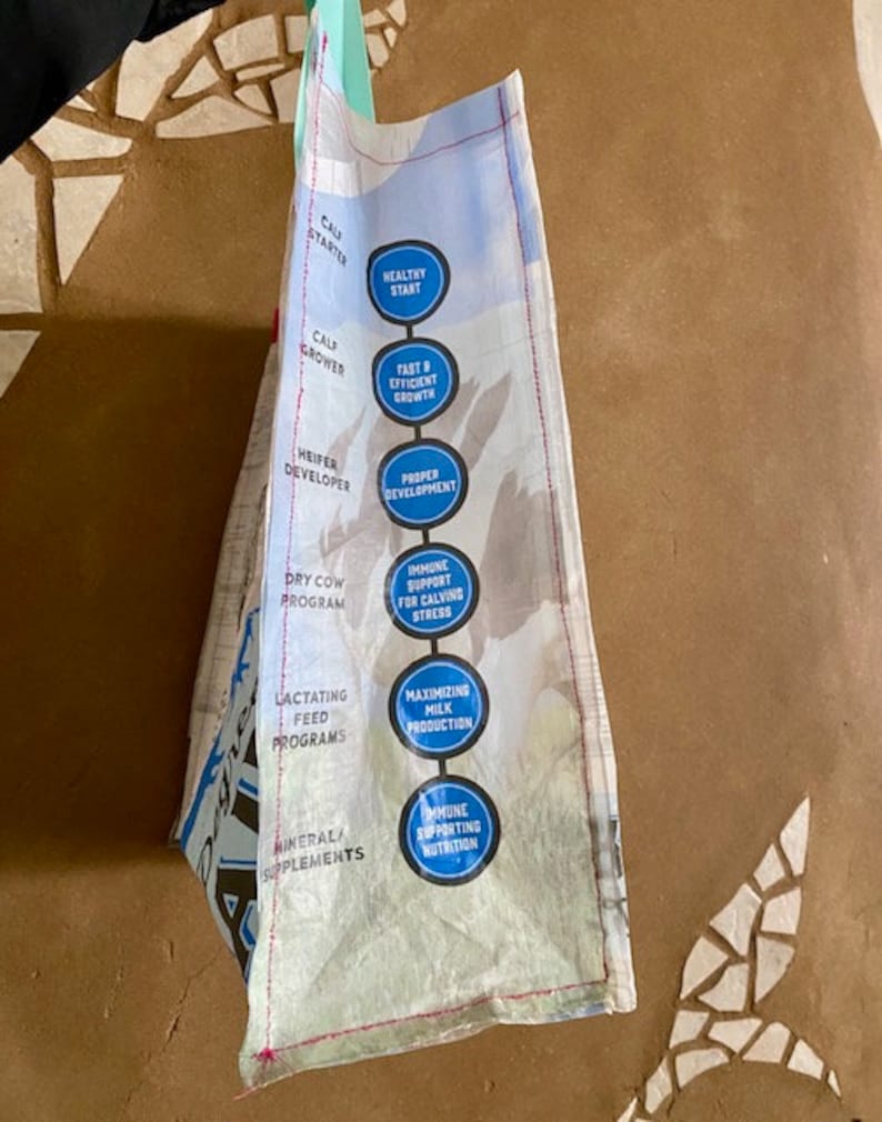 May include: A white bag with blue circles containing text about different stages of cow development. The text includes "Calf Starter", "Healthy Start", "Fast & Efficient Growth", "Proper Development", "Dry Cow Programme", "Immune Support for Calving Stress", "Lactating Feed Programmes", "Maximizing Milk Production", "Mineral Supplements", and "Immune Supporting Nutrition".