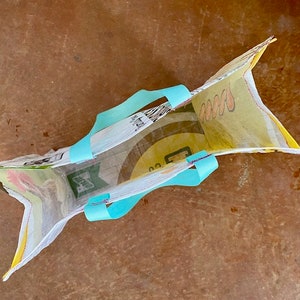 May include: A reusable shopping bag made from recycled plastic with a yellow and green floral print. The bag has turquoise blue handles.