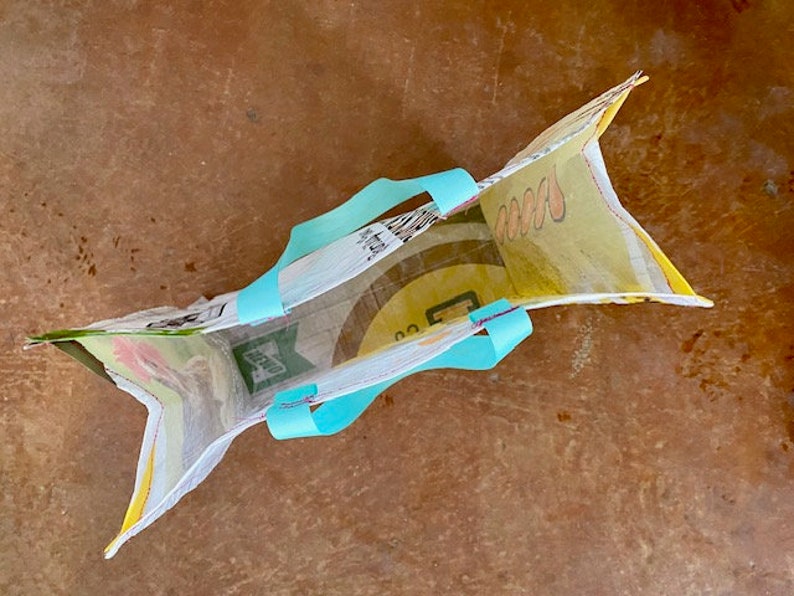 May include: A reusable shopping bag made from recycled plastic with a yellow and green floral print. The bag has turquoise blue handles.