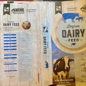 May include: A brown and white bag of Degree Dairy Feed with a cow and calf on the front. The bag is labeled with the company name "NEMO" and the text "Commitment to Quality". The bag also includes a nutritional statement and a list of ingredients.