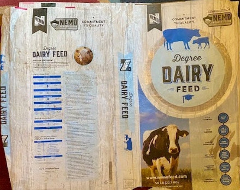 May include: A brown and white bag of Degree Dairy Feed featuring a cow and calf on the front. The bag is branded with the company name "NEMO" and the text "Commitment to Quality". The bag also includes a nutritional statement and a list of ingredients.