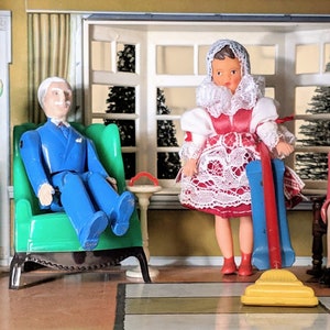 May include: A group of four dolls, two men and two women, are posed in a dollhouse setting. The dolls are dressed in vintage clothing. The woman in the center is holding a yellow and blue toy vacuum cleaner. The dolls are sitting in chairs and standing on a checkered floor.