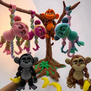 May include: A collection of articulated monkey figurines in various colors including pink, blue, orange, black, and brown, positioned on and around a brown tree structure with green leaves, accompanied by several small yellow banana accessories.