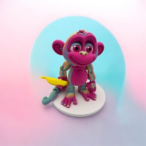May include: A colorful monkey figurine with a yellow banana. The monkey has a pink face, ears, and body, with rainbow-colored arms and legs. It stands on a white circular base against a gradient background of pink and blue.
