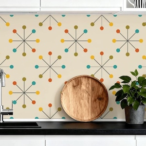 May include: A kitchen backsplash featuring a cream backdrop with a repeating pattern of starbursts in orange, yellow, teal, and olive green. A wooden tray, a potted plant, and a black coffee maker are on the countertop.