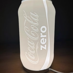 Puede incluir: Lámpara con forma de lata de Coca-Cola Zero blanca con un cable blanco.