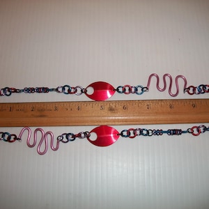 May include: Two handmade bracelets with red, blue, and silver chain links, a red oval center, and a pink wavy design. A wooden ruler shows the bracelets are approximately 10 inches long.