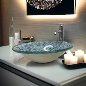 May include: A white ceramic bathroom sink with a blue and white patterned glass bowl. The sink is on a white countertop with two candles on a black tray.