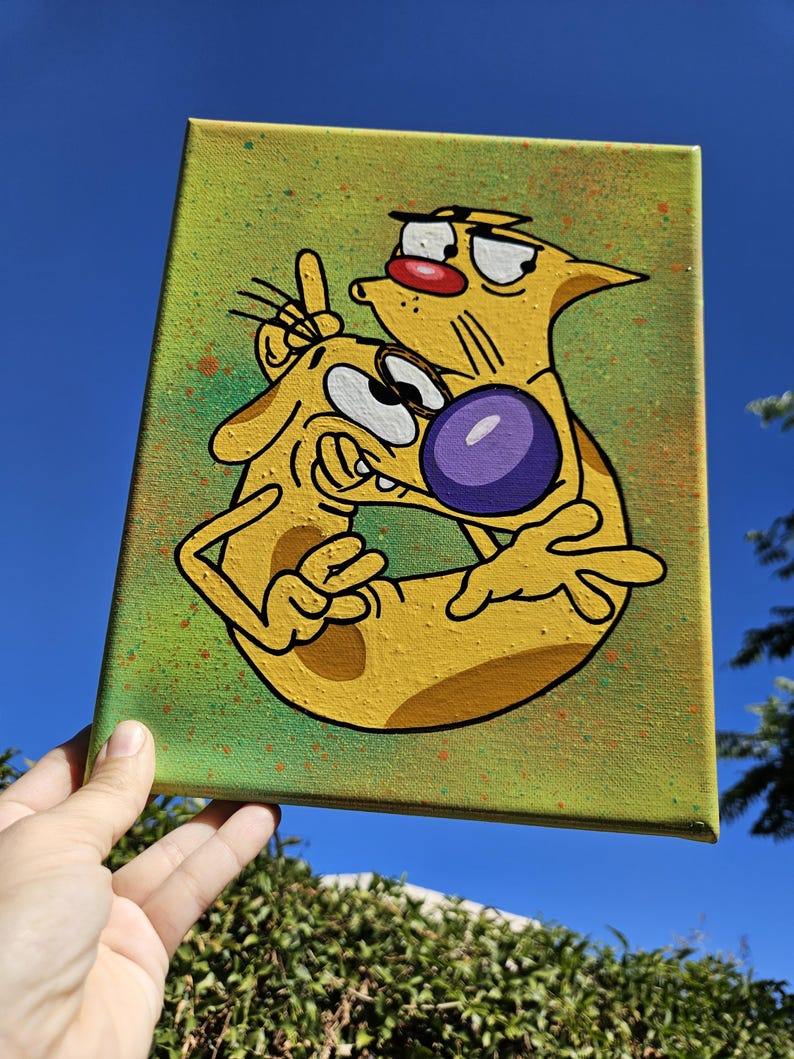 May include: A canvas painting featuring the cartoon characters Cat and Dog. The artwork depicts the characters in a yellow and black color scheme, set against a green background with paint splatters. The characters are embracing, with Dog holding up two fingers.