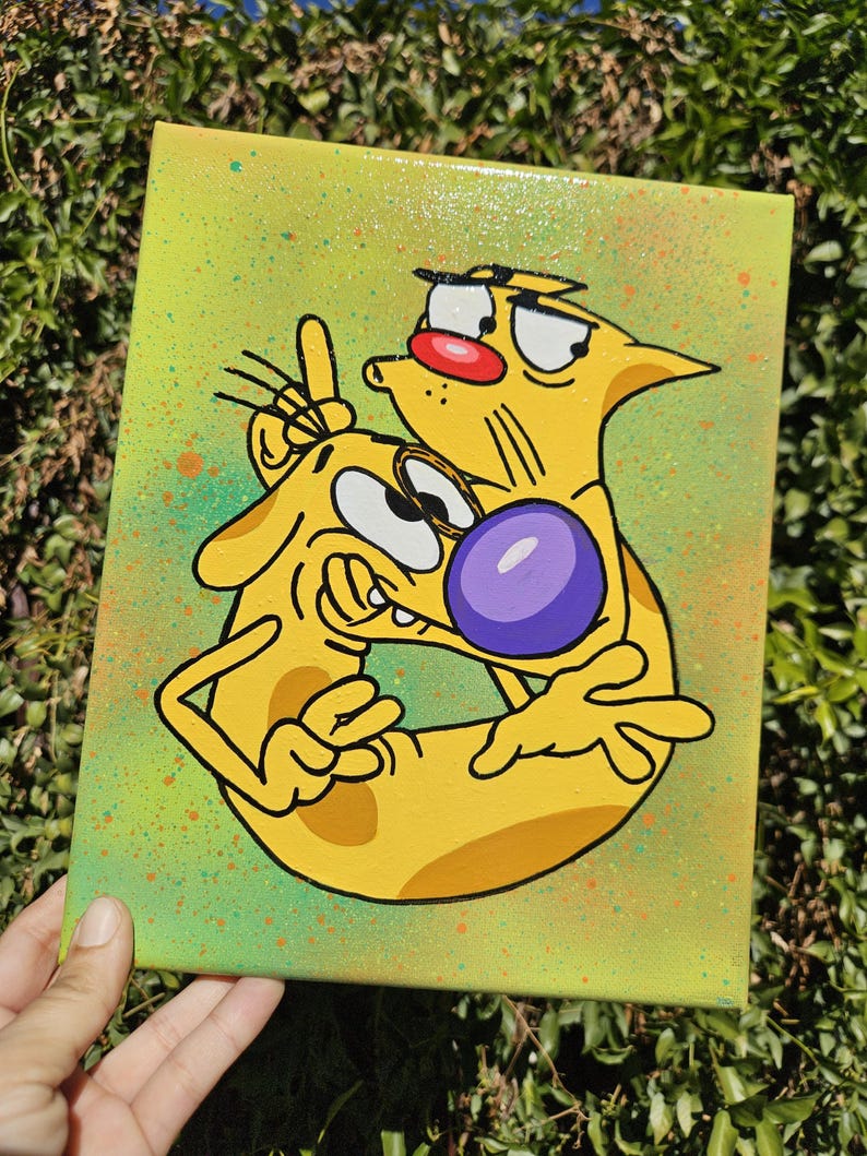 May include: A hand-painted canvas featuring the cartoon characters Cat and Dog. The artwork depicts the characters in a playful embrace, with Cat giving a peace sign. The background is a gradient of green and yellow with colorful paint splatters.