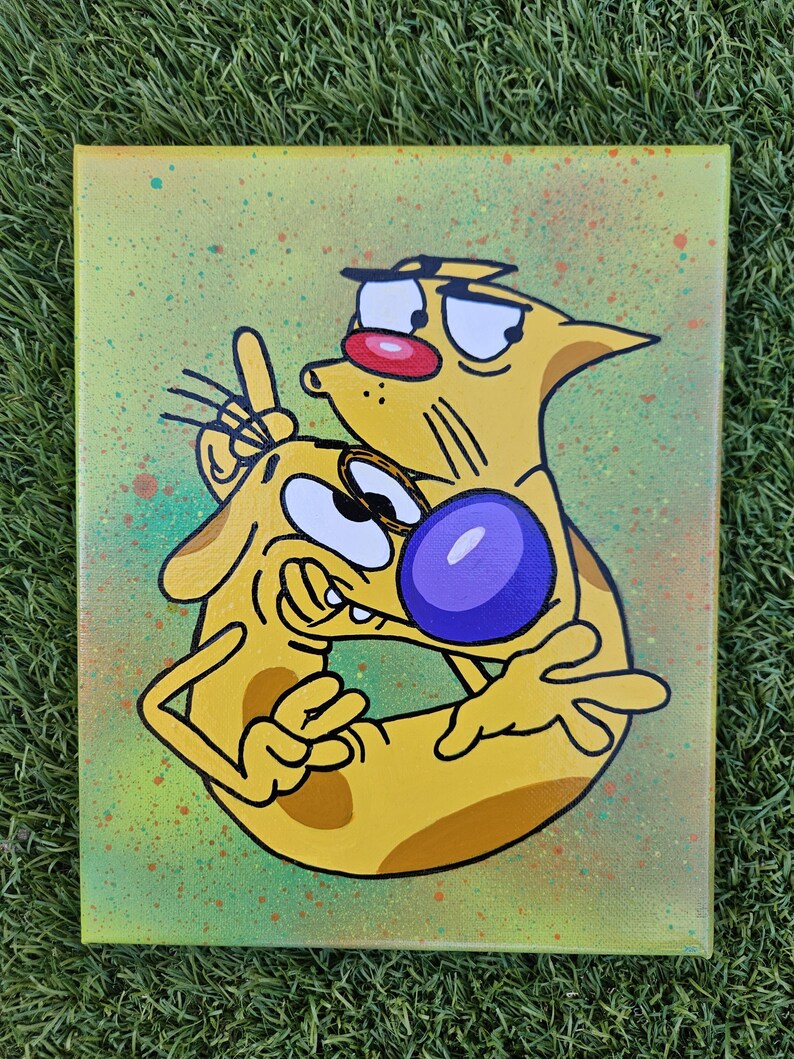 May include: A canvas painting featuring the cartoon characters Cat and Dog. The yellow characters are outlined in black, with Cat having a red nose and Dog with a purple nose. The background is a light green with colorful paint splatters.