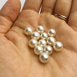 May include: A hand holding a group of white round pearls.