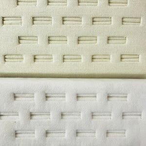 Puede incluir: Dos bandejas de exhibición de anillos blancas con múltiples ranuras para anillos. La bandeja superior está hecha de una tela texturizada y la bandeja inferior está hecha de una tela lisa.