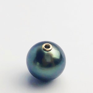 Puede incluir: Una perla redonda de color verde oscuro con un bucle de metal dorado en la parte superior.