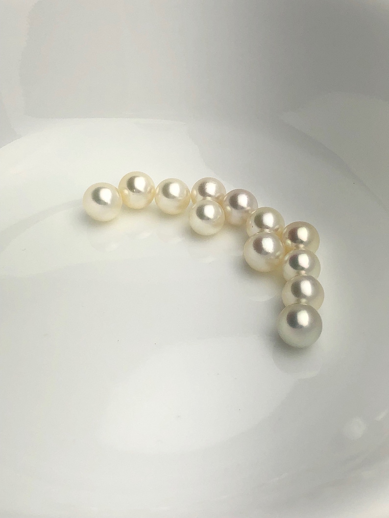 May include: A collection of white pearls arranged in a curved line on a white surface.