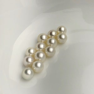 May include: A group of white pearls arranged in a triangular shape on a white surface.