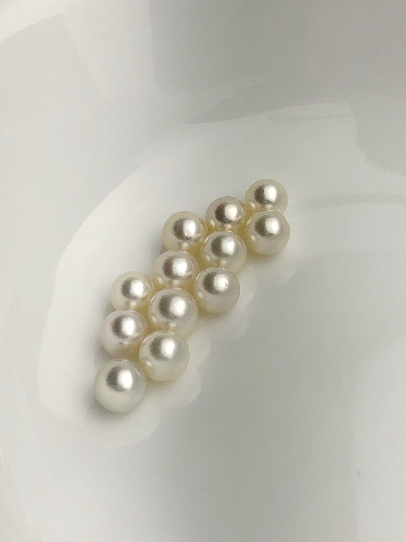 May include: A group of white pearls arranged in a triangular shape on a white surface.