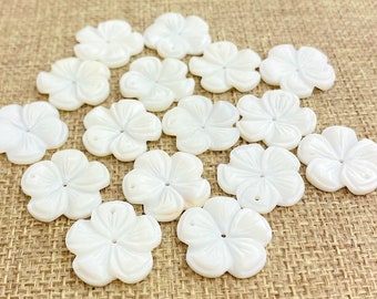 May include: A collection of 14 white, mother-of-pearl flower-shaped buttons. The buttons have a raised, three-dimensional design and a hole in the center.
