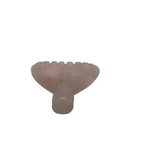 Puede incluir: Una herramienta gua sha rosa claro en forma de corazón, con un borde dentado y un mango redondeado. La herramienta está hecha de piedra lisa y pulida, diseñada para masajes faciales y cuidado de la piel.
