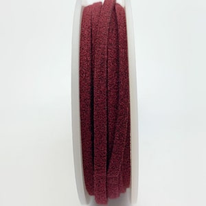 Puede incluir: Un carrete de cordón de ante burdeos, enrollado alrededor de una bobina de plástico blanco.