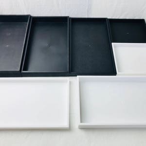 Puede incluir: Un juego de seis bandejas rectangulares, tres negras y tres blancas. Las bandejas son todas del mismo tamaño y forma, y están dispuestas en dos filas de tres.