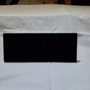 Puede incluir: Un expositor rectangular de terciopelo negro con múltiples agujeros para sujetar pendientes.