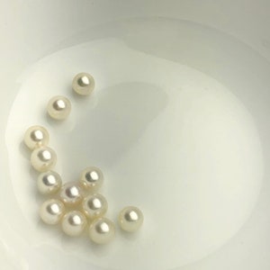 May include: A collection of white pearls in a white bowl. The pearls are round and smooth.