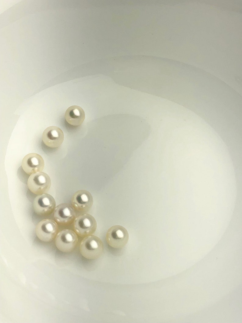 May include: A collection of white pearls in a white bowl. The pearls are round and smooth.