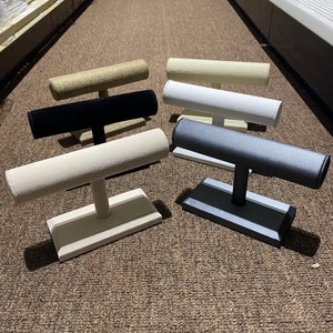 May include: Five different jewelry display stands with a padded top and a base. The stands are made of wood and have a variety of colors, including beige, black, white, and gray.