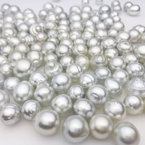 May include: A large collection of white, round pearls of varying sizes. The pearls are scattered on a white surface.