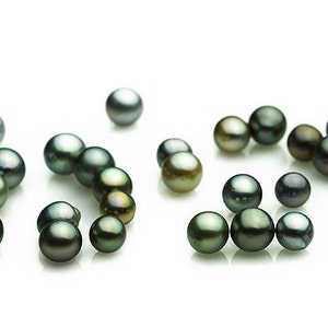 Puede incluir: Una colección de perlas de color verde oscuro y negro esparcidas sobre una superficie blanca.