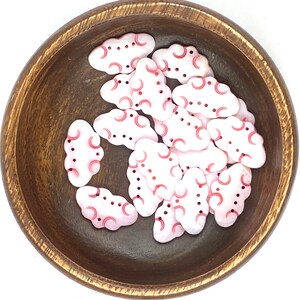 Peut inclure: Un bol de boutons en forme de nuage rose et rouge avec un fond blanc. Les boutons ont un motif en relief de cercles et de demi-cercles rouges.