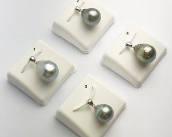 Può includere: Quattro ciondoli d'argento con perle a forma di goccia di colore grigio scuro. Le perle sono su supporti di esposizione bianchi.
