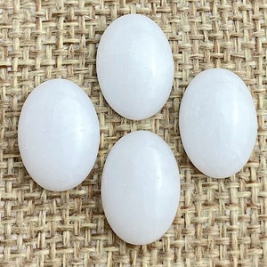 May include: Four white oval-shaped stones on a brown burlap background. The stones are smooth and have a slightly iridescent sheen.
