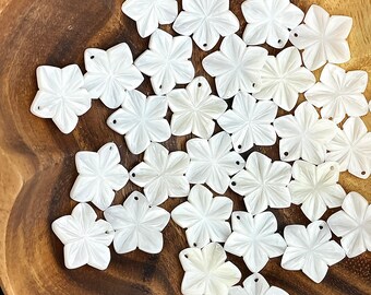 May include: A bowl filled with white, shell-shaped flower charms. The charms have a delicate, carved design and are perfect for jewelry making or crafting.