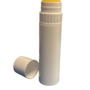 Op de afbeelding: Een witte plastic tube met gele lippenbalsem. De tube is open en de dop is eraf.