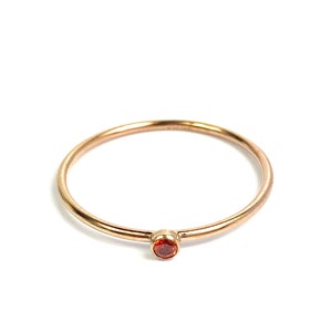 May include: A delicate gold ring with a small, round, orange gemstone.