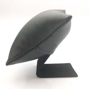 May include: Black leather watch display stand with a pillow-shaped top and a rectangular base.